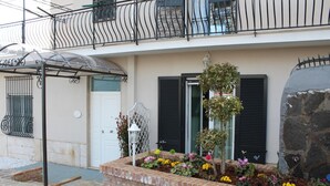 A two-story building with a balcony, a covered outdoor seating area, and a flower bed in front of the entrance.