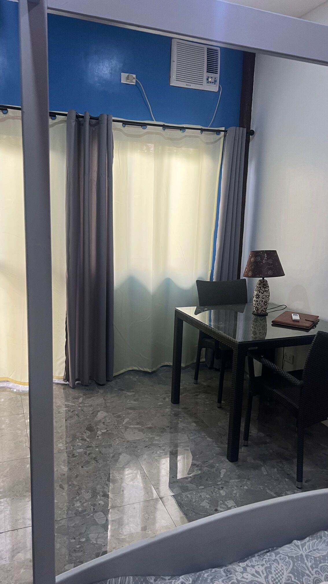 Una habitación pequeña con una mesa, sillas, una lámpara y una ventana con cortinas.