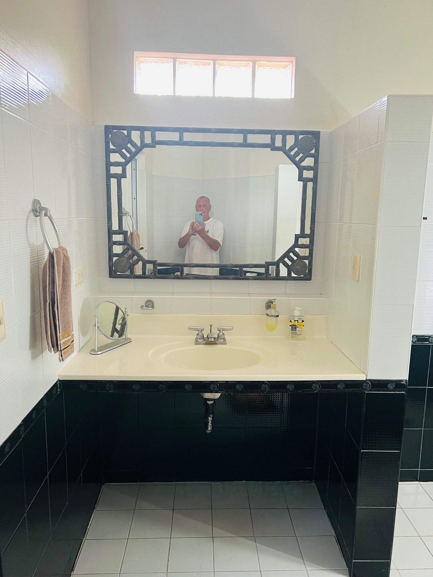 Un baño con un espejo grande, un lavamanos y una ventana sobre el espejo.