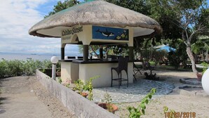 A beachside kiosk named 'Cabiltao Sunset Beach Resort' with a thatched roof, seating area, and potted plants. - Cabilao Sunset Dive & Beach Resort (Loon)