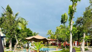 A pool area with lounge chairs and a table, surrounded by well-maintained grass and palm trees. - Cabilao Sunset Dive & Beach Resort (Loon)