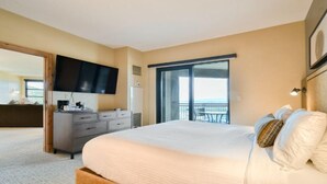 A hotel room with a large bed, a flat-screen TV mounted on the wall, a dresser, and a balcony with a view.