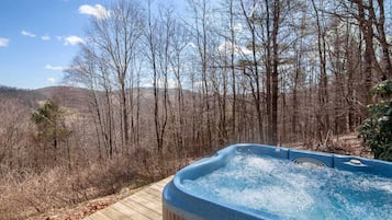 Un bain à remous sur une terrasse en bois, entouré d’une zone boisée, avec une montagne en arrière-plan.