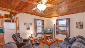 A cozy living room with a fireplace, leather chairs, a television, and a wooden ceiling. - Cozy 3BR Cabin w/ Long-Range Views, Hot Tub & Dog-Friendly (Todd)