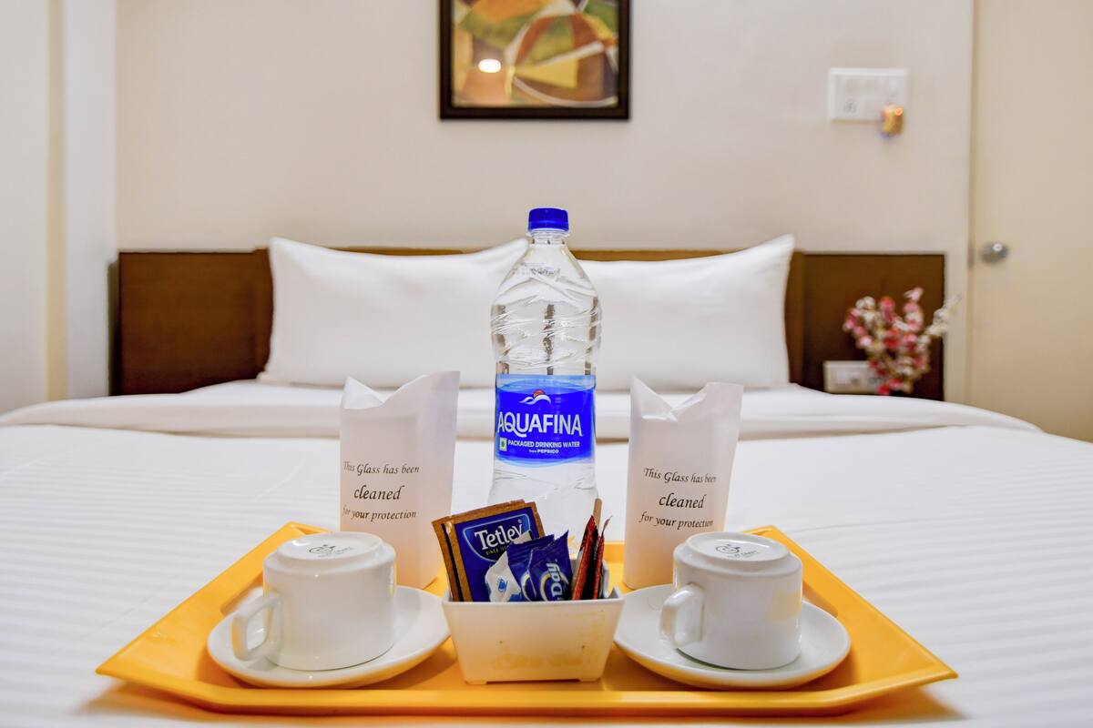 A hotel room with a bed, a tray with two cups and a bottle of Aquafina water, and a box of Tetley tea bags.