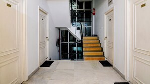 A hallway with white doors numbered 202 and 203, leading to a staircase with a black railing and wooden steps. - The Inn (Kolkata)