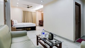 A hotel room with a bed, a sofa, a coffee table with a kettle, a water bottle, and a chair. - The Inn (Kolkata)