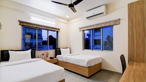 A hotel room with two beds, a ceiling fan, an air conditioning unit, and large windows with night views. - The Inn (Kolkata)