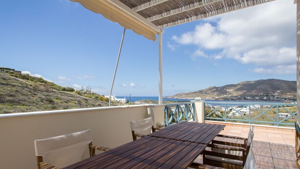 Ein Holztisch mit Stühlen auf einem Balkon mit Blick auf das Meer und die Hügel.