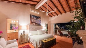 A bedroom with a bed, a nightstand, a mirror, a painting, and a balcony with a view of the city.