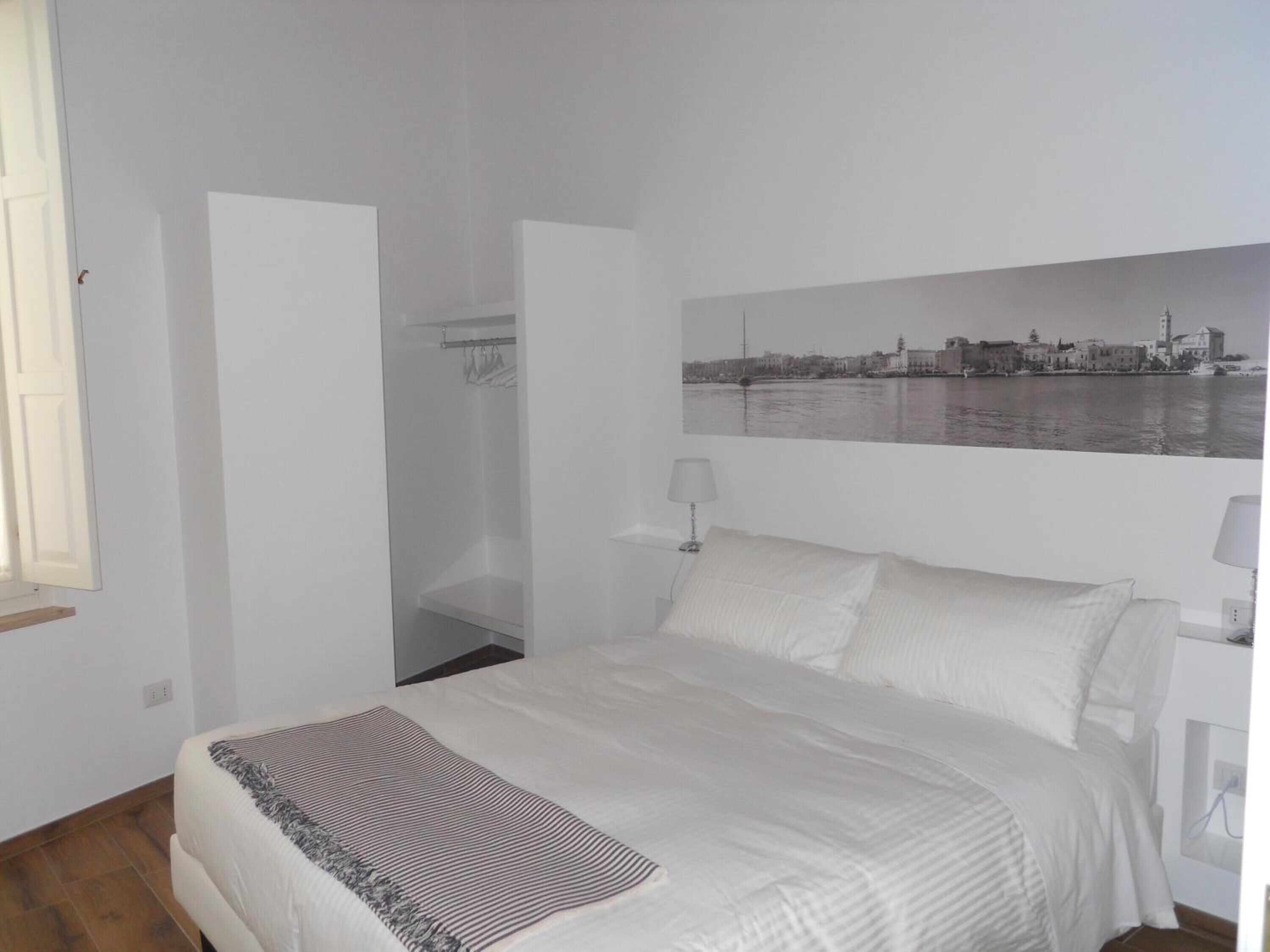 A bedroom with a bed, a closet, a window, and a cityscape painting on the wall.