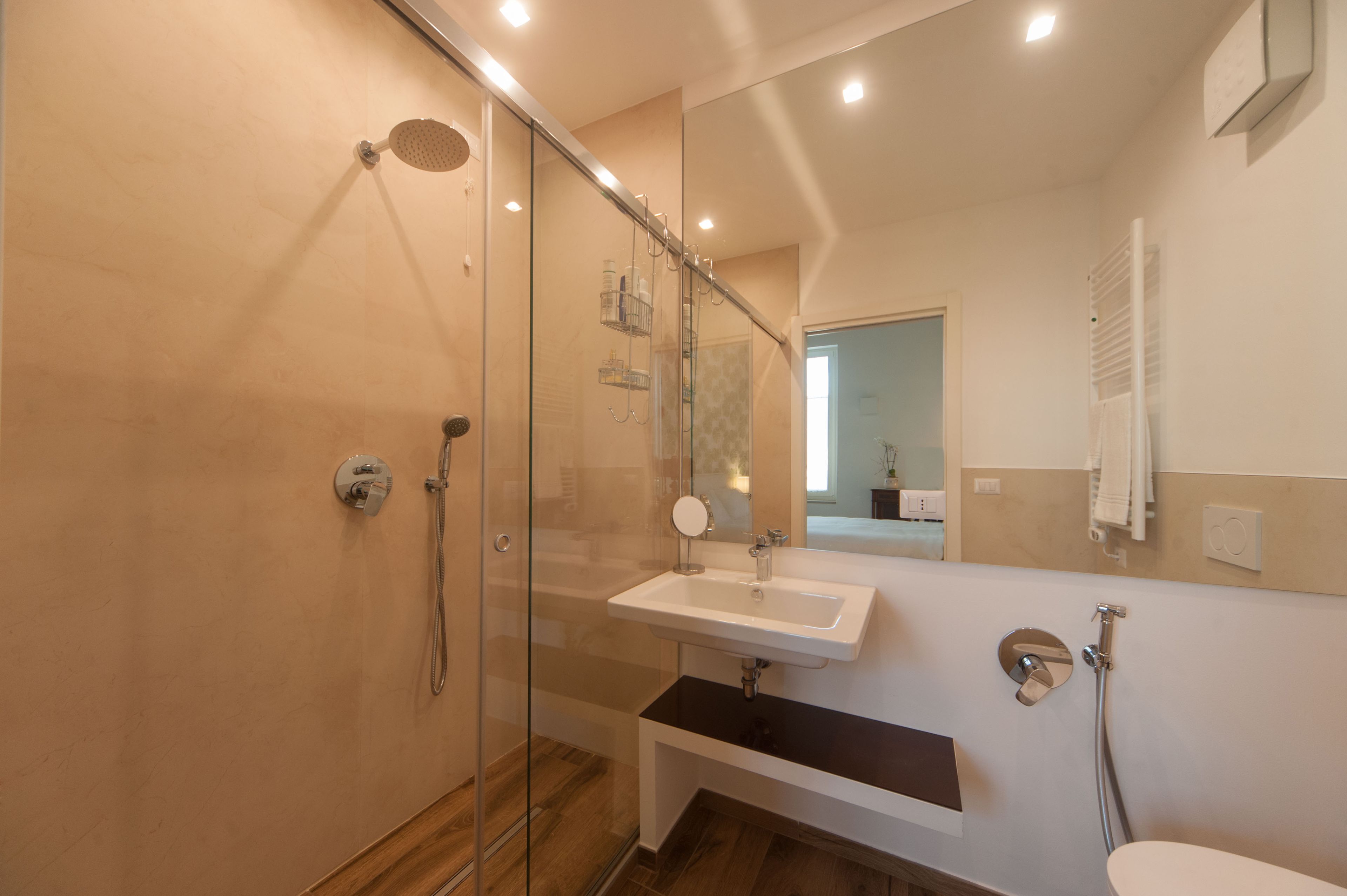 Een moderne badkamer met een douche met glazen wand, een wit wastafeltje en een spiegel erboven.