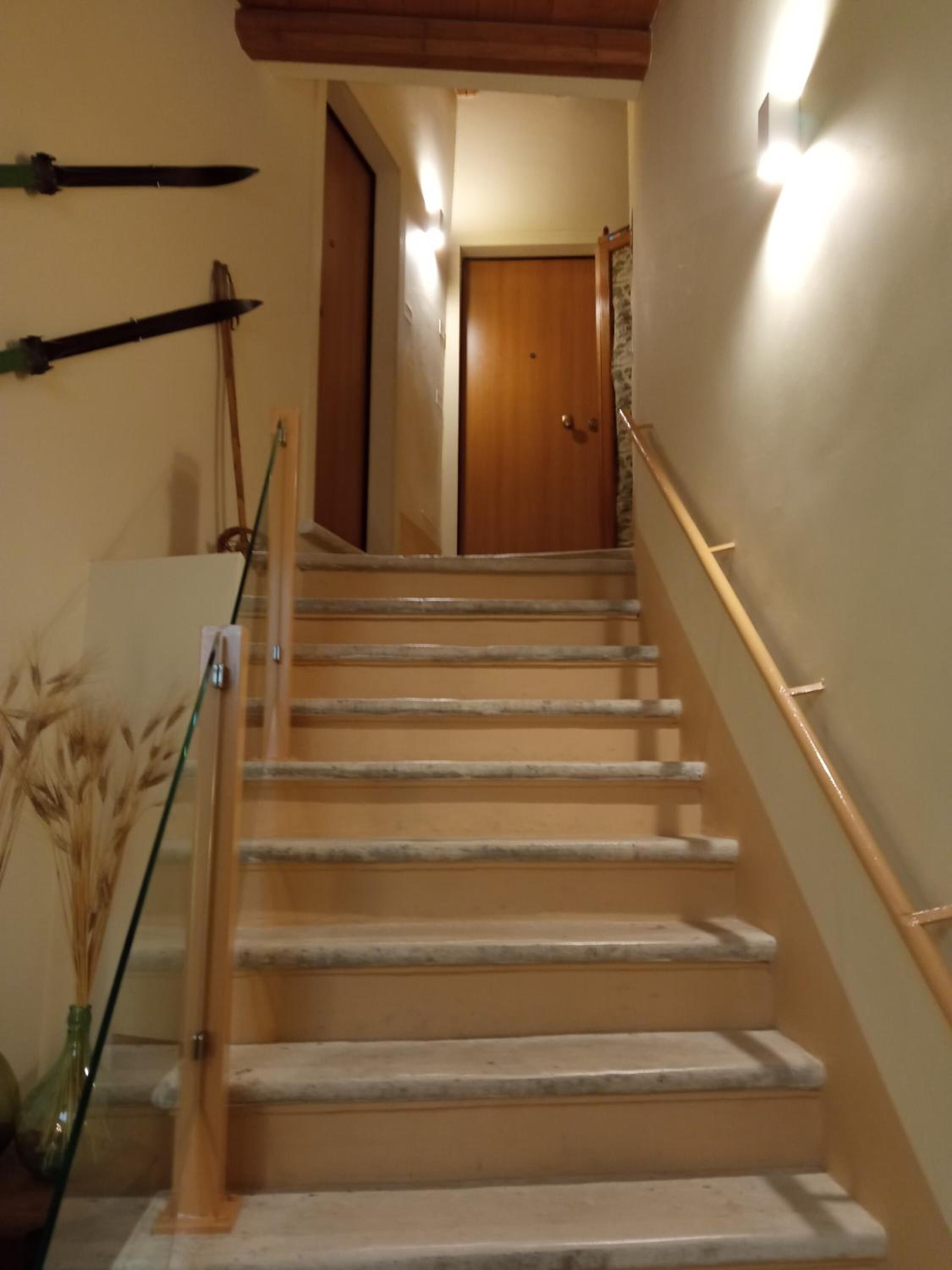 A staircase with wooden handrails and a glass railing, leading to a door at the top.