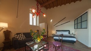 Una habitación acogedora con cama, sofá, mesa de centro y sillón. Hay una ventana con cortinas, una lámpara y un jarrón con flores.