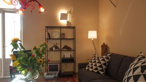 Una sala de estar con un sofá, una mesa de centro de vidrio, una estantería y una lámpara decorativa.