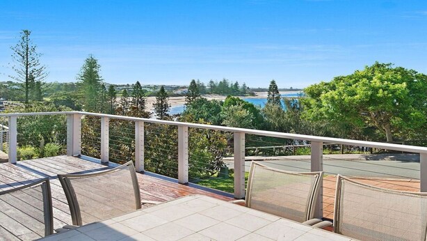 Un balcon doté d’un espace salon extérieur, offrant une vue panoramique sur un paysage verdoyant, avec des arbres et une étendue d’eau.