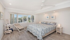 Une chambre avec un grand lit, un ventilateur de plafond et une fenêtre équipée de stores.