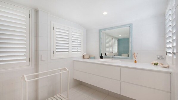 Une salle de bain moderne avec des éléments d’équipement blancs, un grand miroir et un porte-serviettes.