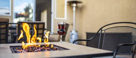 Uma lareira com uma taça de vinho tinto sobre uma mesa, rodeada por cadeiras.