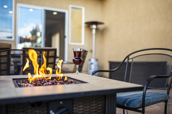 A fire feature with a glass of red wine on a table, surrounded by chairs.