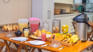 Una mesa de desayuno con diversas frutas, una cafetera y una jarra de jugo.