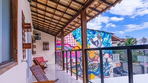 Un espacio al aire libre techado con suelo de baldosas, bancos de madera y un mural colorido en la pared.