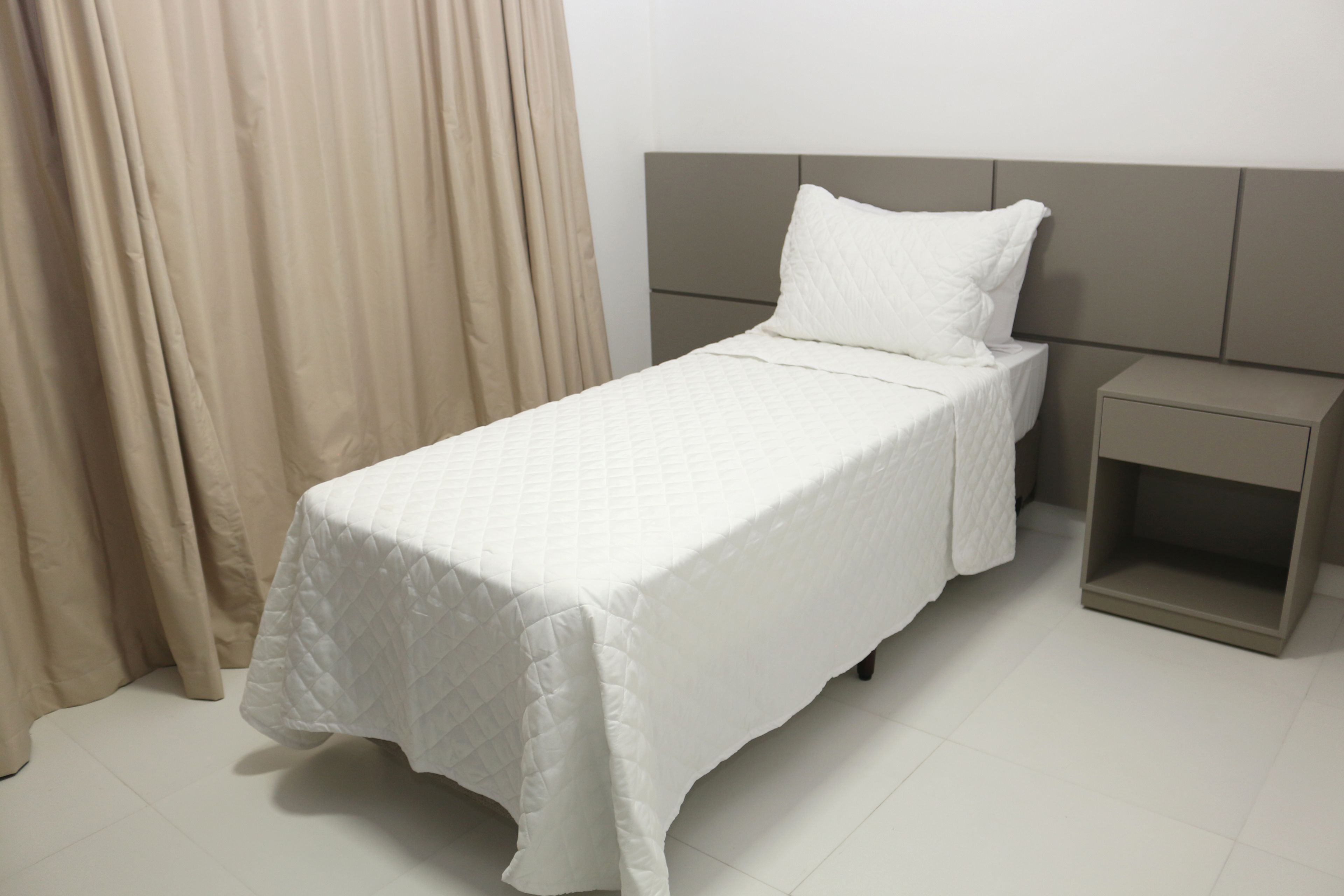 Una cama bien hecha con una colcha blanca acolchada, un cojín a juego y un cabecero gris.