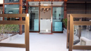 Una entrada de edificio moderna con puertas de vidrio, fachada de madera y un pequeño jardín.