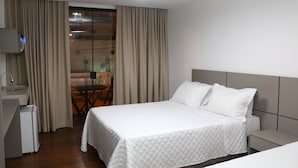 Habitación de hotel con cama, mesita de noche y vistas a un balcón.