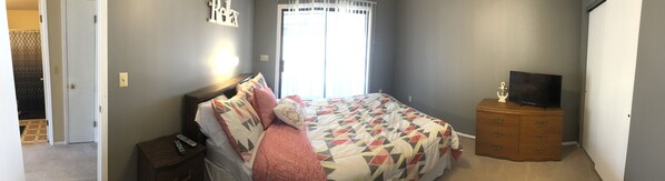 Un dormitorio con cama, cómoda, televisor y ventana con cortinas.