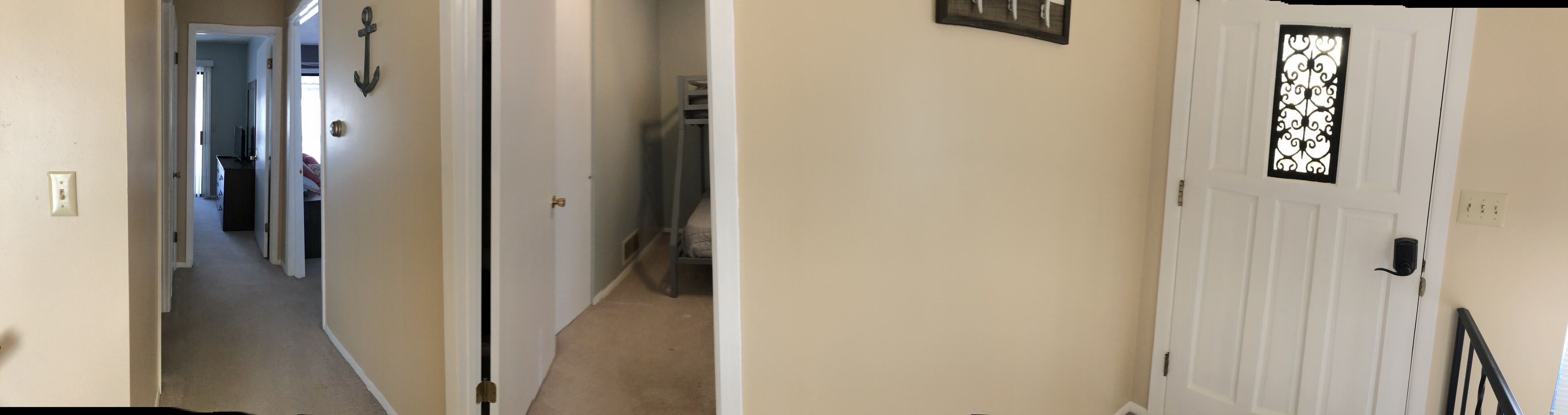 A hallway with a door on the right, a coat rack, and a bed in the background.