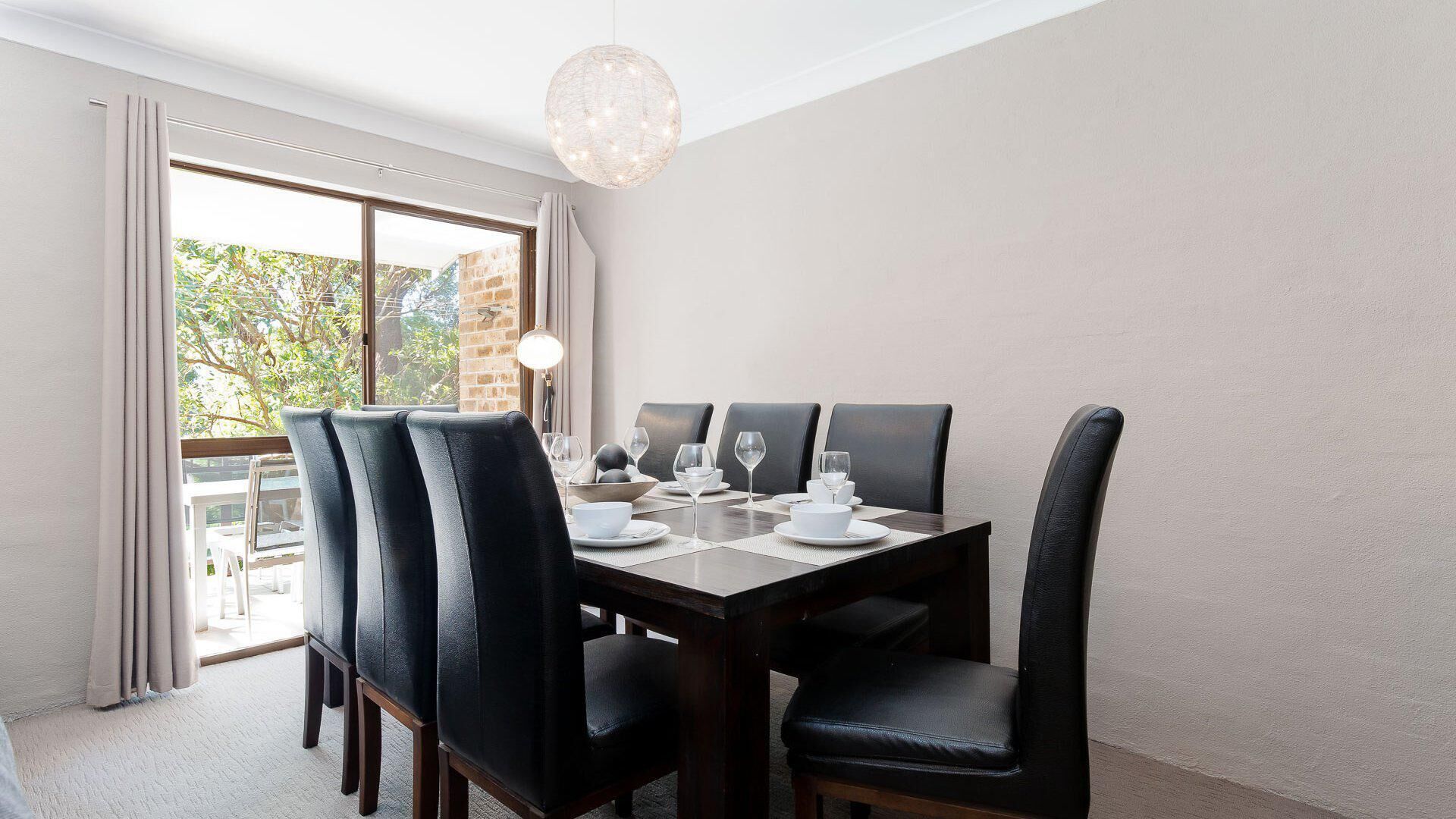 A dining room with a rectangular table set for six, surrounded by black leather chairs.