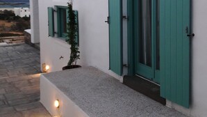 Un edificio moderno con paredes blancas y contraventanas verde azulado, que cuenta con un pequeño jardín con una planta en maceta.
