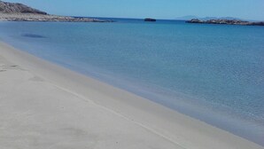 Una playa con agua azul cristalina, una orilla arenosa y afloramientos rocosos a lo lejos.