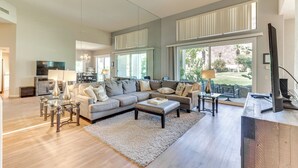 Amplia sala de estar con un sofá seccional grande, una mesa de centro y un televisor. Hay un comedor con una mesa y sillas, y una cocina con estufa y alacenas.