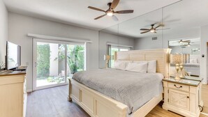 Un dormitorio con una cama, mesitas de noche, un ventilador de techo y un ventanal grande.