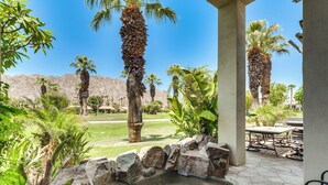 Un patio con una fuente de piedra, palmeras y vistas a un paisaje montañoso.