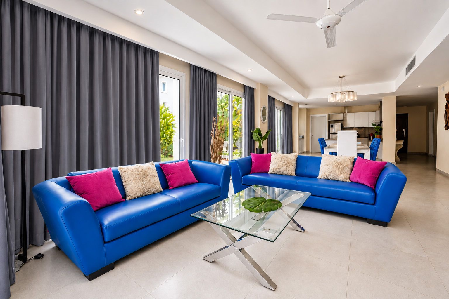 Ein modernes Wohnzimmer mit zwei blauen Sofas, einem Glastisch und einem Deckenventilator.