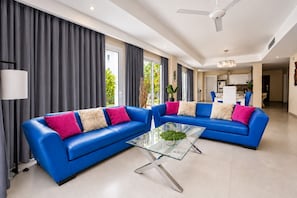 Een moderne woonkamer met twee blauwe banken, een glazen salontafel en een plafondventilator.