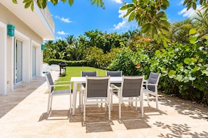 Une terrasse extérieure avec une table et des chaises, entourée d’une végétation luxuriante et sous un ciel bleu dégagé.