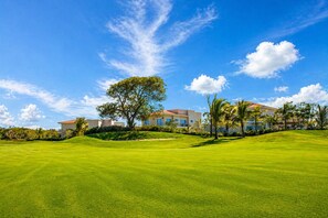 A golf course with a large tree and a building in the background.
