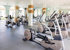Une salle de sport équipée de nombreux appareils de cardio, notamment des tapis de course et des elliptiques, disposés en rangées.