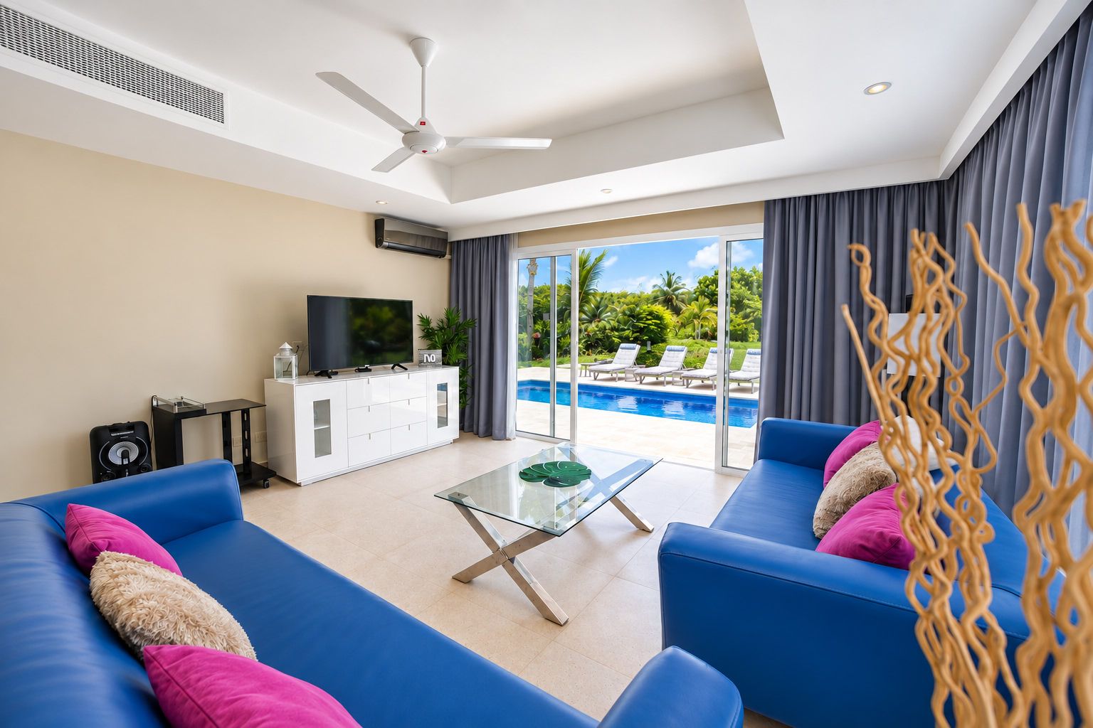 A modern living room with a blue sofa set, a glass coffee table, and a television on a white cabinet.