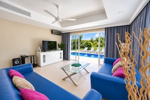 A modern living room with a blue sofa set, a glass coffee table, and a television on a white cabinet.