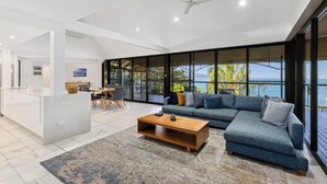 A modern living room with a large sofa, a coffee table, and a dining area. - Mermaids Reach, Stunning House on Hamilton Island (Hamilton Island)