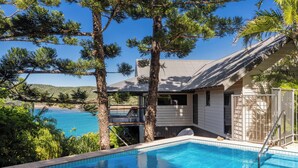 A swimming pool with a view of the sea, surrounded by trees and a building with a balcony. - Mermaids Reach, Stunning House on Hamilton Island (Hamilton Island)