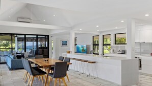 A modern kitchen with a central island, bar stools, and a dining area with a table and chairs. - Mermaids Reach, Stunning House on Hamilton Island (Hamilton Island)
