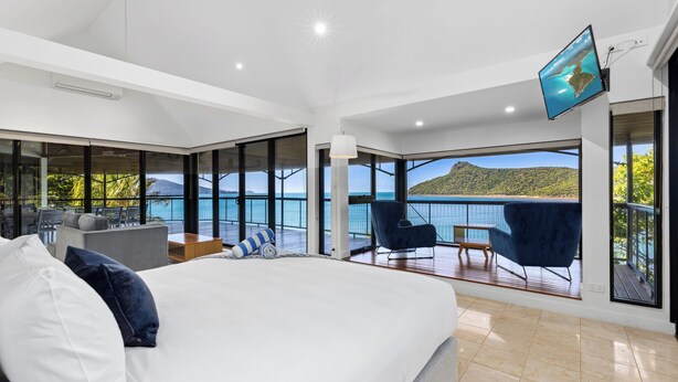 A modern bedroom with a large bed, a TV mounted on the wall, and a balcony with a view of the sea. - Mermaids Reach, Stunning House on Hamilton Island (Hamilton Island)
