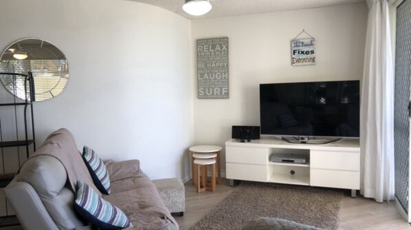 A living room with a sofa, a television, a small round table, and a wall with motivational quotes. - 1 Edmund Shores 3-BR Kings Beach Apt w/ Pool (Kings Beach)