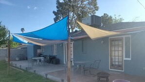 Un'area patio con un telo parasole blu, mobili da esterno e una grande pianta in vaso.